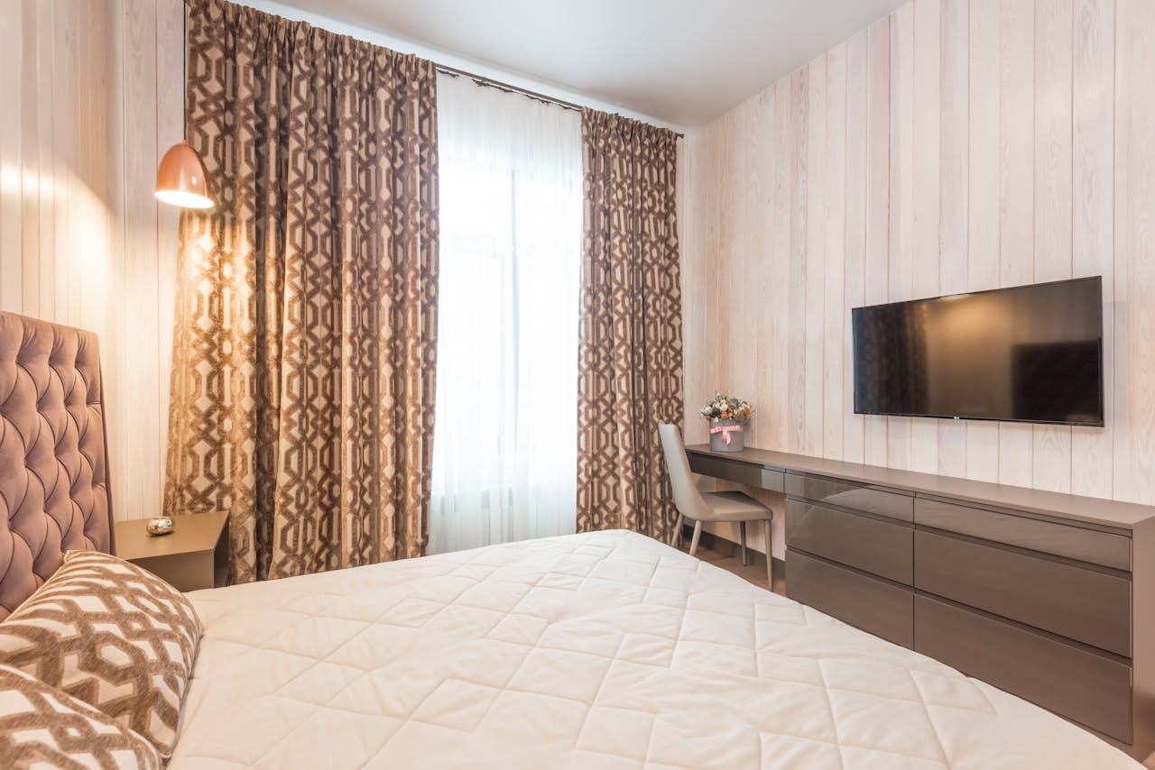 gallery-01 Comfortable bed with soft cushions and headboard in classic styled bedroom with modern TV set and chair