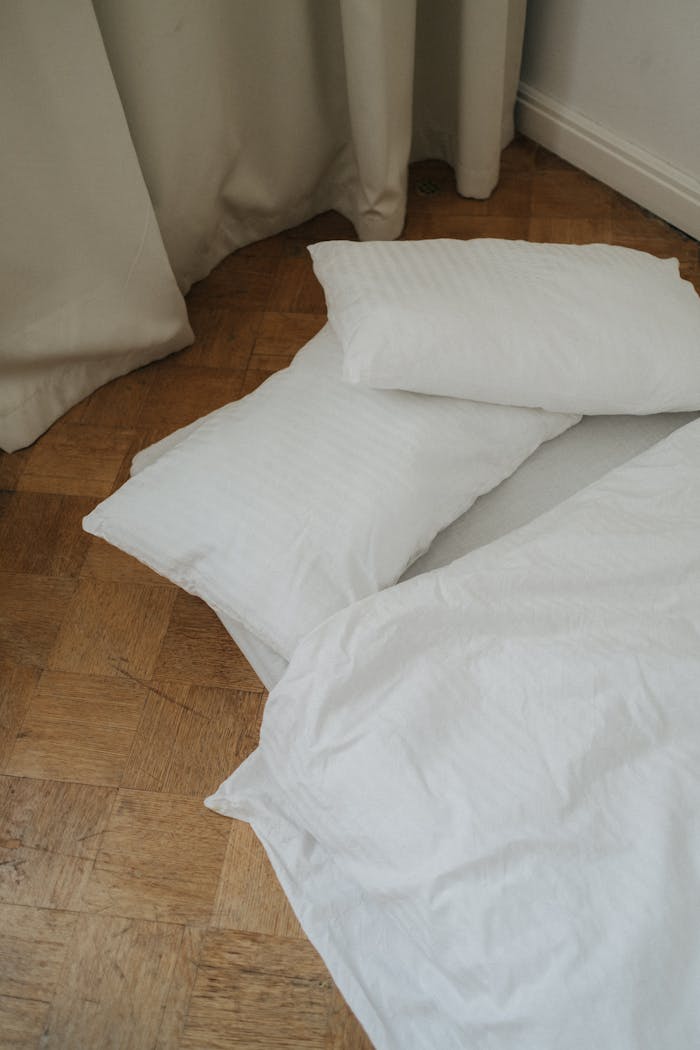 our-story A simple minimalist setup with white bedding and pillows on a wooden floor, emphasizing simplicity and calm.